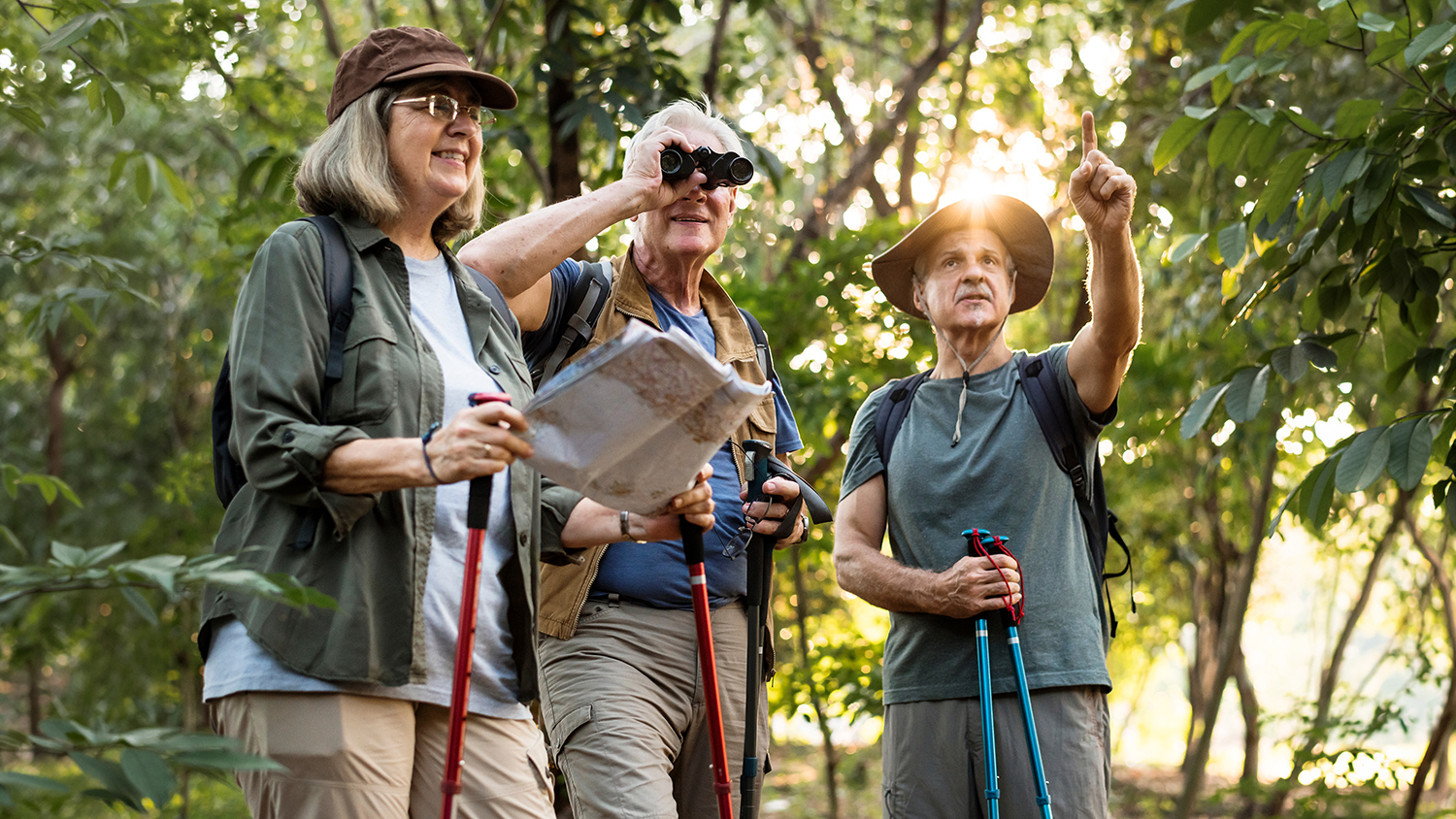 Three Bird Watchers Exploring A Wooded Area While Using Binoculars & a Map.
